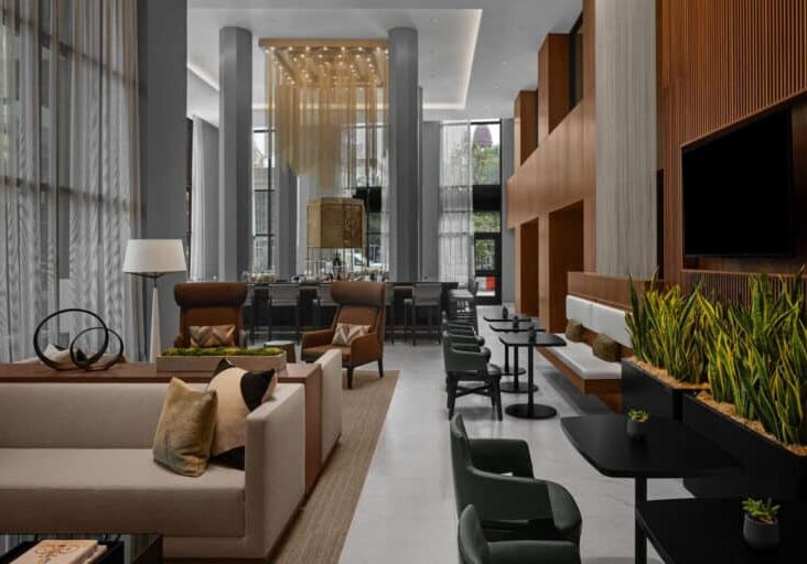 Hotel flooring installation in A modern hotel lobby with an elegant interior design, featuring a blend of soft beige sofas, dark wood paneling, plush green chairs, and ambient lighting that creates a welcoming and stylish atmosphere.